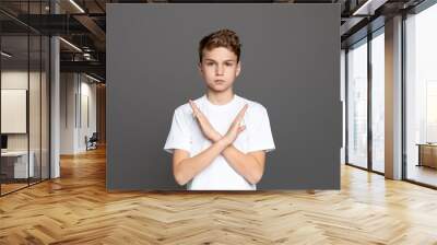 Teenager with arms crossed in an X shape, showcasing refusal or denial, isolated on a grey background Wall mural