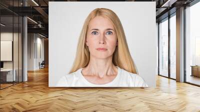 This image shows a woman with blonde hair looking directly at the camera with a neutral expression. She is wearing a white t-shirt and has a light complexion. The background is a plain white wall. Wall mural