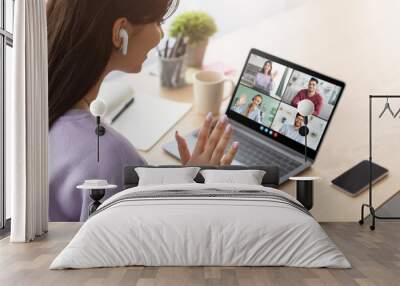 This image shows a young woman participating in a video conference meeting at home. She is wearing a purple sweatshirt and has her hand raised to the camera, as if she is about to speak. Wall mural