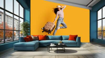 Time To Travel. Cheerful Young Woman Wearing Wicker Hat Jumping With Suitcase Wall mural