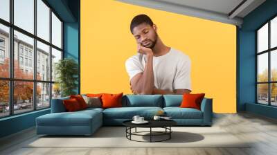 Tired african american guy leaning on his hand and sleeping after overworking, standing over yellow background Wall mural