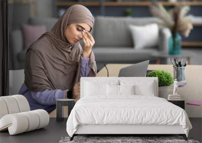 Tired muslim woman sitting at desk, rubbing dry irritated eyes Wall mural