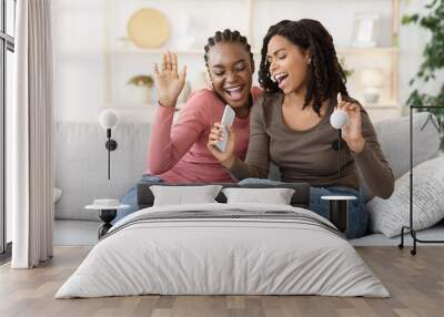 Two cheerful young female friends singing at home Wall mural