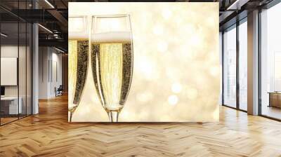 Two elegant glasses filled with sparkling champagne stand together, capturing the festive atmosphere created by a shimmering golden backdrop, perfect for celebrations and special occasions. Wall mural