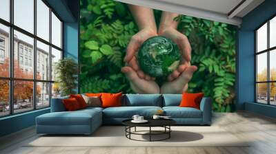 Two hands delicately hold a miniature green earth in front of vibrant green leaves. Wall mural