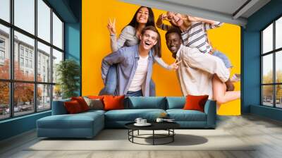 Two international teen couples having fun over yellow background Wall mural