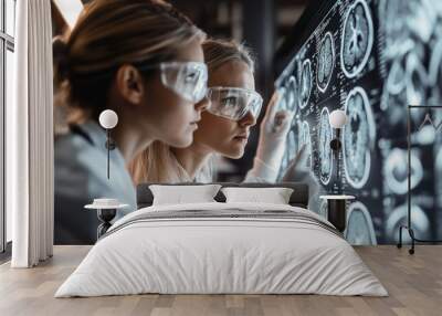 Two women in lab coats and goggles examine detailed brain scans on a large screen, focused on their research and findings. Wall mural