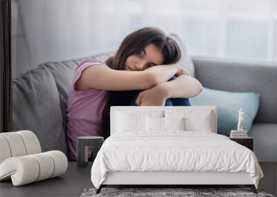 Unhappy teen girl feeling depressed or desperate, sitting on couch at home, suffering from problem or teenage depression Wall mural