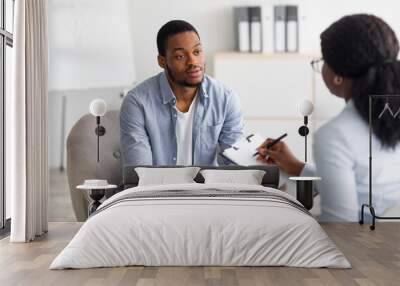 Unhappy young black man having session with professional psychologist at mental health clinic Wall mural