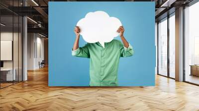 Unrecognizable african american young guy holding an empty speech bubble in front of his head, blue background Wall mural