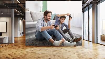 Videogames concept. Joyful father and son competing in online games, holding joysticks while sitting on carpet Wall mural