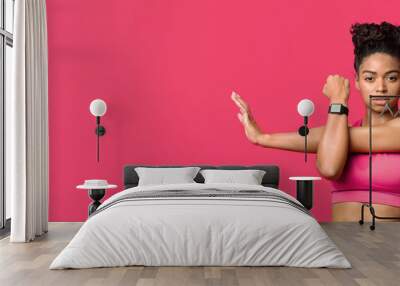 Warming up. Portrait of young sporty black girl doing stretching exercise over red background, copy space Wall mural