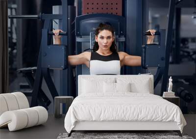 Weightlifting exercises. Millennial woman working out on training machine at sports club Wall mural