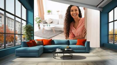 Welcome. Portrait of cheerful woman standing in doorway of modern apartment, greeting visitor and inviting guest to enter her home, happy smiling young lady holding door looking out flat Wall mural