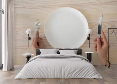 White empty plate and female hands holding silver fork and knife on wooden table background, top view Wall mural