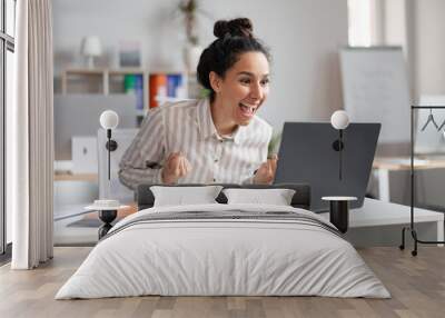 Win. Emotional excited businesswoman celebrating success, shaking clenched fists and looking at laptop in office Wall mural