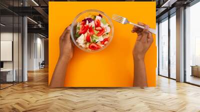 Woman eating fresh vegetable salad on orange background Wall mural