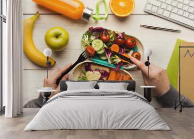 Woman eating healthy dinner from lunch box at her working table Wall mural