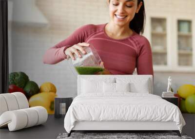 Woman In Fitwear Pouring Green Smoothie In Glass At Kitchen Wall mural