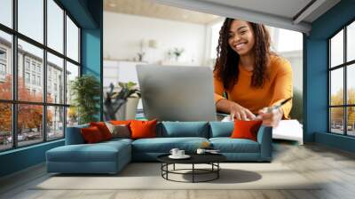 Woman sitting at desk, using computer and writing in notebook Wall mural