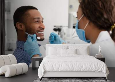 Young african guy smiling to his female dentist while having treatment at modern clinic Wall mural