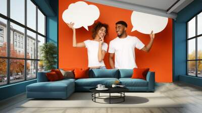 Young black couple holding speech bubbles on orange background Wall mural