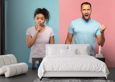 Young black woman gesturing hush sign, holding finger near mouth, man screaming and clenching fist at camera Wall mural