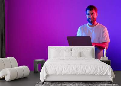 Young caucasian guy using laptop in studio with neon light Wall mural