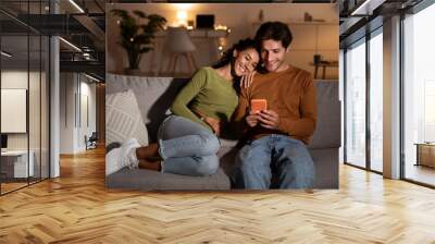 Young Couple Using Phone Browsing Internet Relaxing Sitting At Home Wall mural