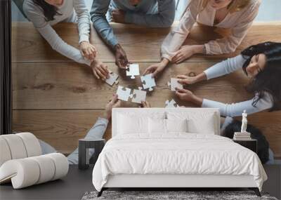 Young creative team sitting around table, putting together puzzle pieces Wall mural