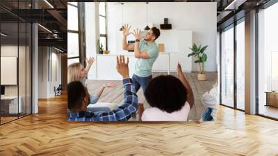 Young diverse friends playing charades game at home. Arab guy showing pantomime riddles, his fellow students guessing Wall mural