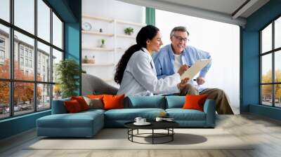 Young doctor asking senior impaired male patient in wheelchair to sign insurance policy at home Wall mural