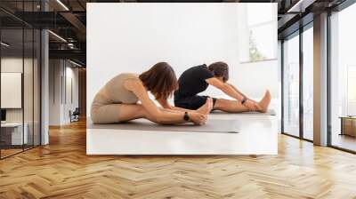 Young european couple in sportswear do exercising, stretching legs, practicing yoga Wall mural