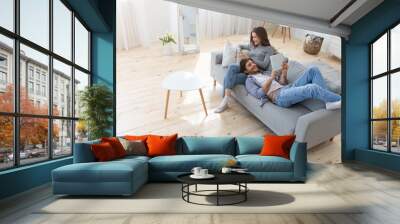 Young family of two relaxing on sofa at home Wall mural