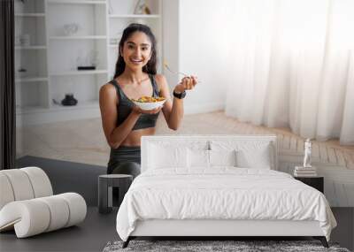 Young indian woman eating healthy salad after workout Wall mural