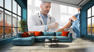 Young lady getting vaccinated against coronavirus, male doctor making injection in shoulder for female patient Wall mural