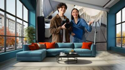 Young male photographer talking with female art director, preparing for photo shooting, standing near lighting equipment Wall mural