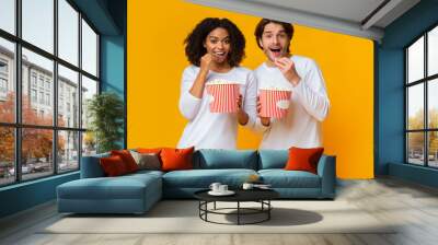 Young multiracial couple eating popcorn from buckets and looking at camera Wall mural