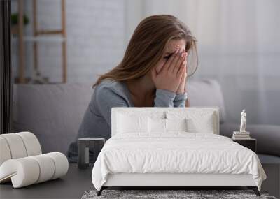 Young woman burying her face in hands and crying, feeling depressed or desperate on sofa indoors Wall mural