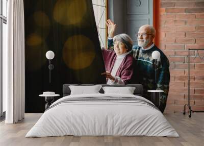 An elegant old couple in a Christmas studio. Grandparents in a cute sweaters. Family standing near window Wall mural