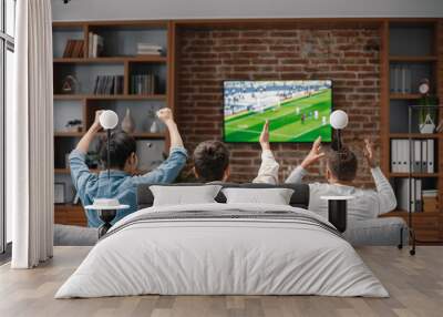 Back view of men watching a football game on tv and sitting on a sofa Wall mural