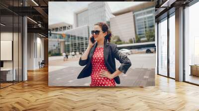 Beautiful businesswoman in a city. Businesswoman in a elegant dress. Lady in a city. Pretty girl with phone. Brunette in a sunglasses. Wall mural