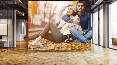 couple sitting on the ground in the city by the autumn leaves Wall mural