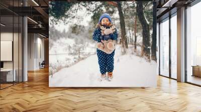 Kid in a winter forest. Girl in a blue hat. Child playing with toy Wall mural