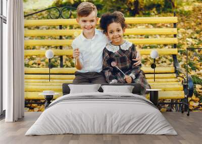 little beautiful dark-skinned girl sitting in the autumn park with her European little friend Wall mural