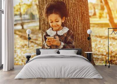 little beautiful dark-skinned girl walks in the autumn park with phone Wall mural