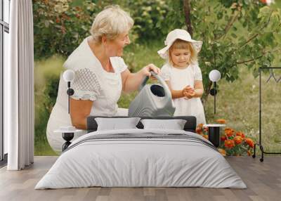 Little girl and her grandmother watering flowers in garden Wall mural