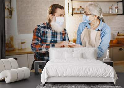 Old couple in a kitchen. Woman in a blue shirt and aprone. People in a medical masks. Wall mural