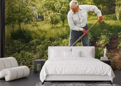 Senior gardener is enjoying his work in garden. Old man in a white shirt. Wall mural