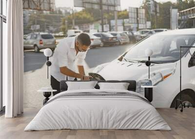 Young Arab man recharging white electric car Wall mural